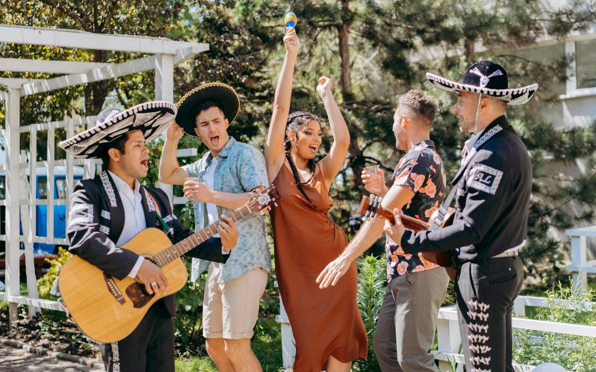 A lively outdoor scene featuring musicians in traditional attire, a woman dancing, and friends celebrating with drinks.